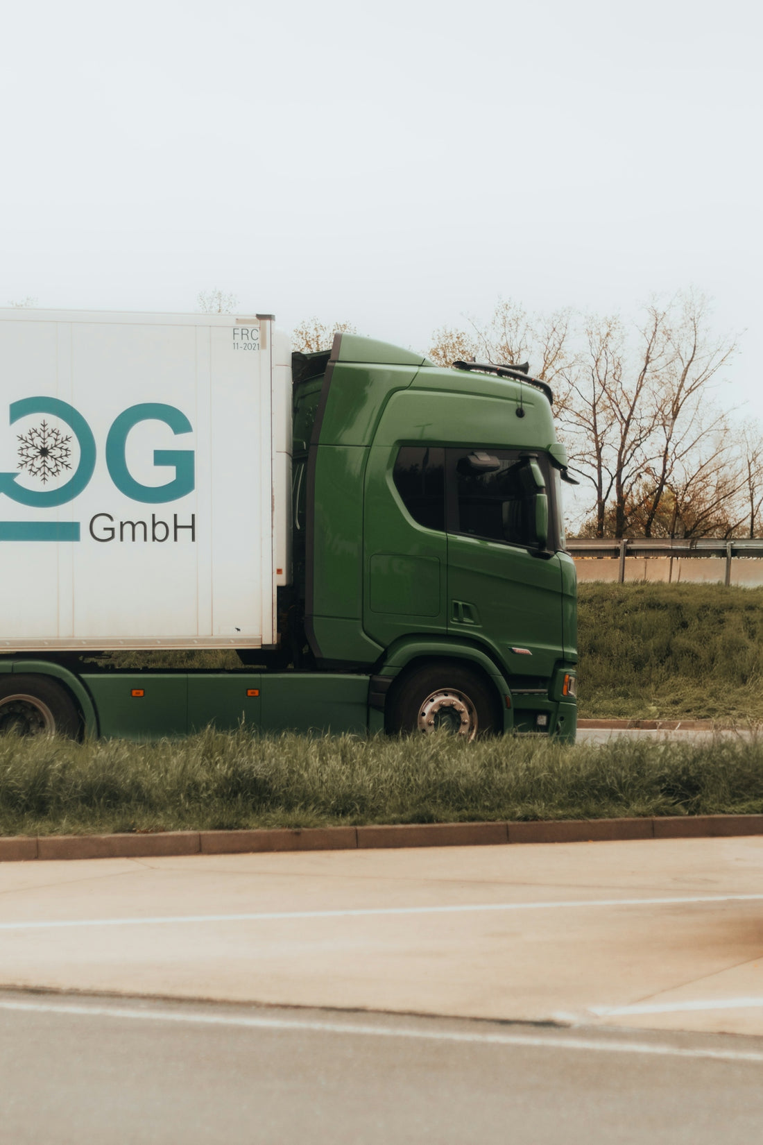 Green truck with white trailer drives on road.
