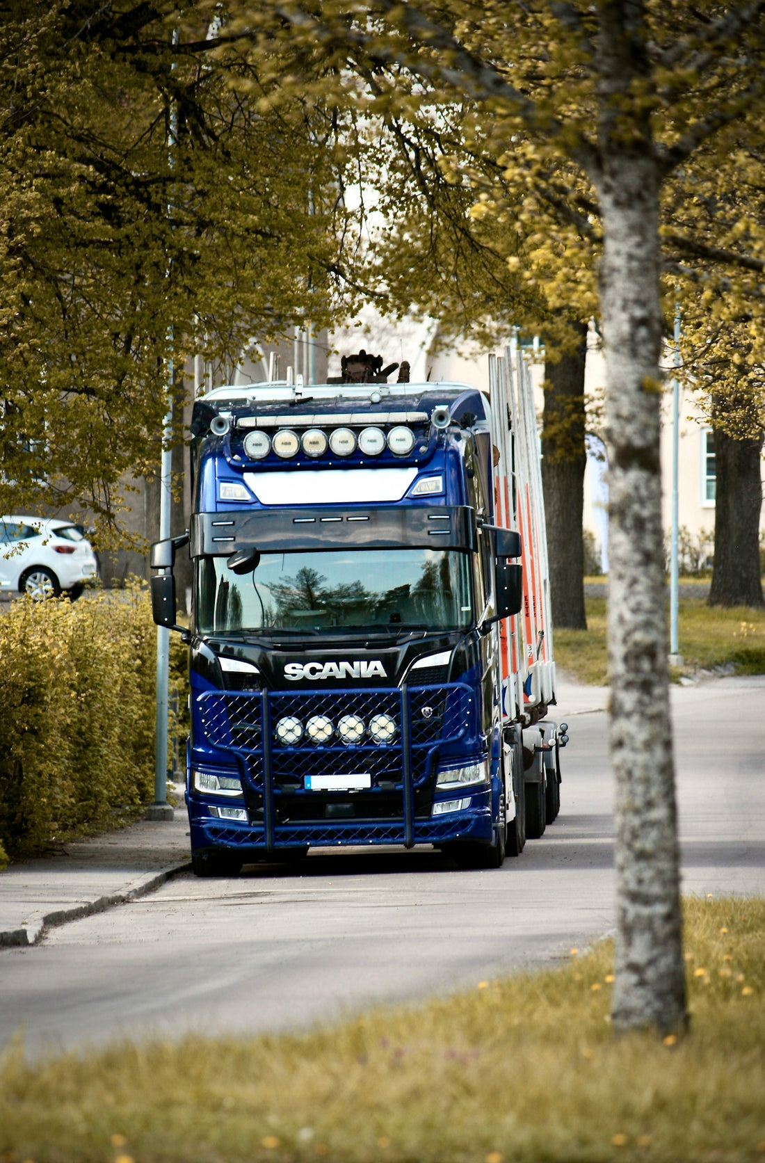 Blue scania truck driving on a street lined with trees.